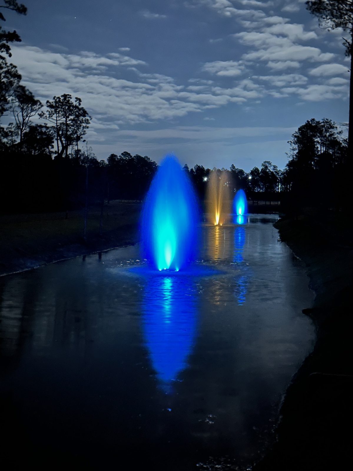 Nighttime fountain scene at Point Preserve with color reflecting across the water
