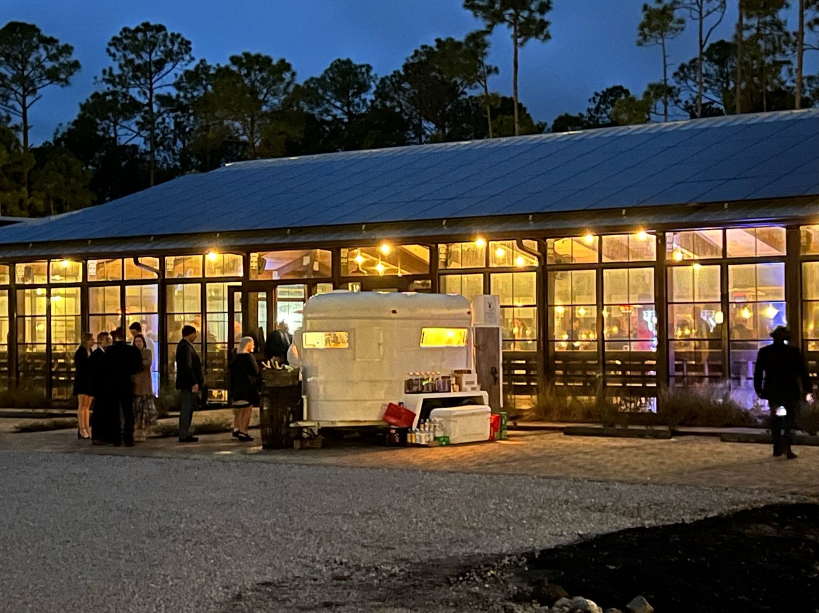 The pavilion glowing warmly at dusk with guests gathering outside